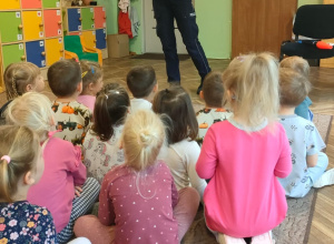 Pani policjantka stoi przed dziećmi, które siedzą na dywanie