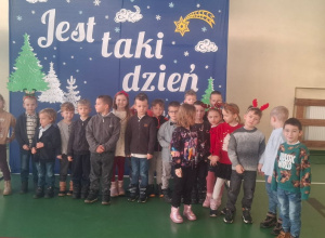 Dzieci stoją w sali gimnastycznej na tle dekoracji świątecznej