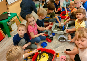 dzieci mieszają w naczyniach ziemię i piasek z wodą