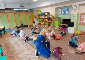 Dzieci i mamy wykonują w pozycji leżącej ćwiczenie na dywanie