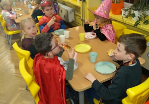 Dzieci przy stolikach jedzą kolację