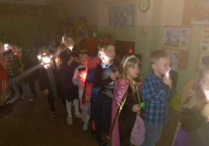 Dzieci w ciemności z latarkami idą zwiedzać przedszkole