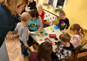 Dzieci z rodzicami przy stolikach robią kartki świąteczne