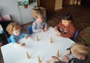 Czworo dzieci z grupy I siedzi przy stoliku i nawleka tasiemkę do świecy