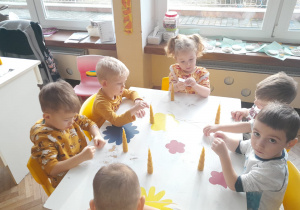Sześcioro dzieci z grupy I siedzi przy stoliku i nawleka tasiemkę do świecy