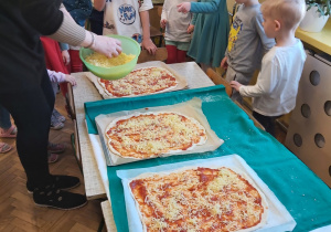 Pani Iza z dziećmi z grupy I i IV nakłada ser na pizzę