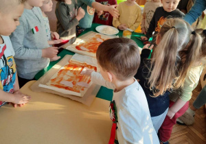 Dzieci z grupy III smarują ciasto na pizzę sosem pomidorowym