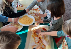 Dzieci z grupy III nakładają ser na pizzę
