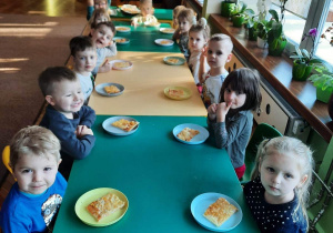 dzieci z grupy III siedzą przy stole z pizzą na telerzykach