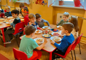 Dzieci z grupy V siedzą przy stoliku i dodają składniki do makaronu