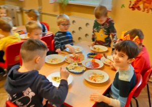 Dzieci z grupy V siedzą przy stoliku i jedzą przygotowane danie
