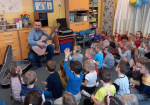 Dzieci słuchają dźwięków gitary wygrywanych przez Pana Piotra