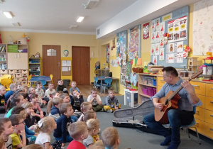 Dzieci słuchają melodii granej na gitarze przez Pana Piotra