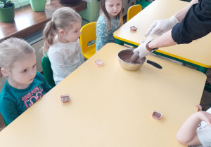 Kilkoro dzieci patrzy, jak prowadzący napełnia strzykawkę płynną czekoladą