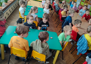 Dzieci siedzą przy stolikach i słuchają informacji o produkcji czekolady