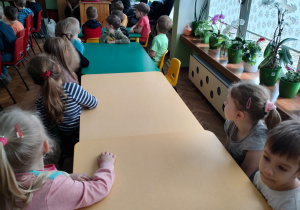 Dzieci siedzą przy stolikach i obserwują, jak prowadząca przygotowuje czekoladę