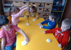 Dzieci z grupy II siedzą przy stolikach i lepią pieczywo z masy solnej