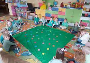 Dzieci z grupy I i III siedzą wokół "kwietnej łąki" z tkaniny
