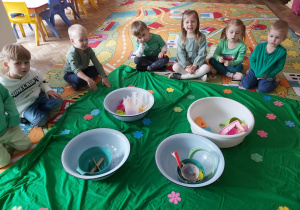 Dzieci z grupy I i III siedzą na dywanie przy miskach z różnymi naczyniami