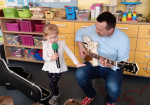 Dziewczynka śpiewa, a pan Piotr gra na gitarze