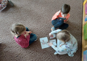 Troje dzieci na dywanie układa obrazek z części