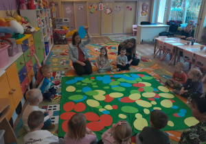 Dzieci z panią Pauliną siedzą na dywanie wokół kolorowych sylwet pisanek
