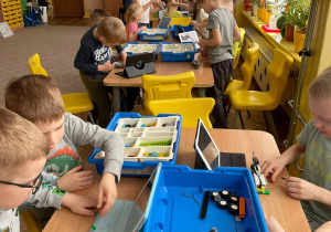 Dzieci przy stolikach budują z klocków Lego według instrukcji na tablecie