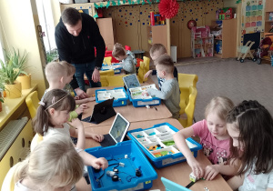 Dzieci przy stolikach budują z klocków Lego według instrukcji na tablecie
