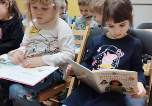 Amelka J. i Laura siedzą na krzesłach i oglądają książki