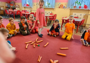 Dzieci z grupy V siedzą na dywanie a Paulinka w środku liczy marchewki