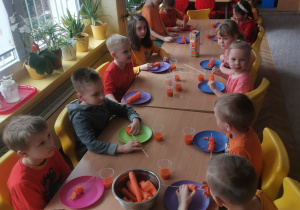 Dzieci z grupy VI przy stole jedzą marchewkę na szaszłyku