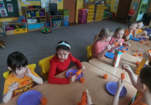 Dzieci z grupy VI przy stole jedzą marchewkę na szaszłyku