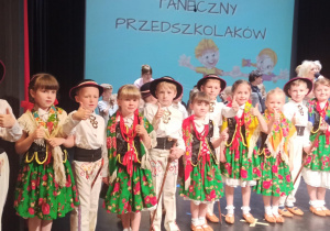Dzieci stoją w szeregu na scenie przed rozdaniem nagród