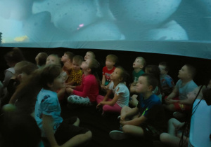 Dzieci siedzą w kapsule i oglądają film
