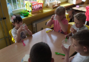 Kilkoro dzieci z grupy VI siedzą przy stole i piją mleko