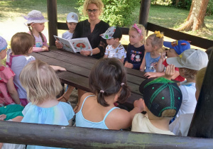 Pani Wiesia z grupy II czyta dzieciom książkę w altance