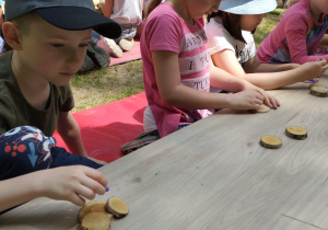Dzieci przy stoliku robią zwierzątko z krążków drewnianych