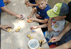 Dzieci przy stoliku robią zwierzątko z krążków drewnianych