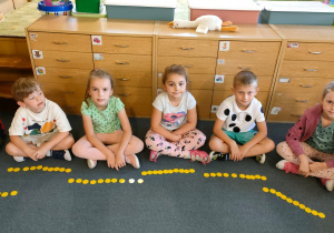 Kilkoro dzieci z grupy Motylki siedzi na dywanie z ułożonymi w rzędzie kropkami