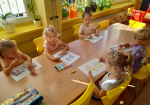 Kilkoro dzieci z grupy Pszczółki siedzi przy stoliku podczas kolorowania kropek na szablonach