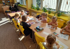 Kilkoro dzieci z grupy Pszczółki siedzi przy stoliku podczas kolorowania kropek na szablonach