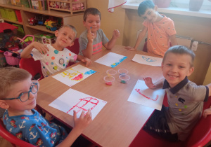 Kilkoro dzieci z grupy Mrówek siedzi przy stoliku podczas malowania kropkowych obrazów