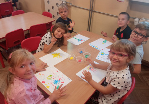 Kilkoro dzieci z grupy Mrówek siedzi przy stoliku podczas malowania kropkowych obrazów