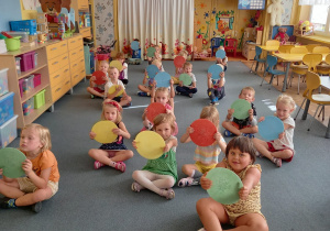 Dzieci z grupy Świetliki siedzą skrzyżnie na dywanie z kółkami w rękach