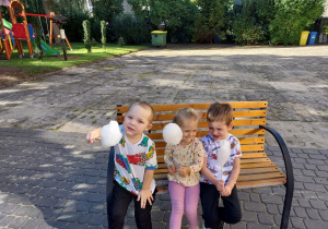 Troje dzieci z grupy Pszczółki siedzi na ławce w ogrodzie z watą cukrową Tekst alternatywny tekst alternatywny