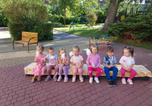 Siedmioro dzieci z grupy Pszczółki siedzi na ławeczce w ogrodzie z watą cukrową