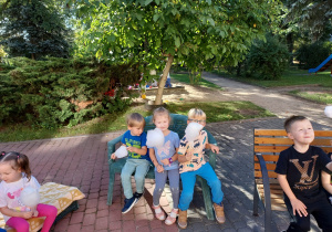 Troje dzieci z grupy Pszczółki siedzi na ławce w ogrodzie z watą cukrową