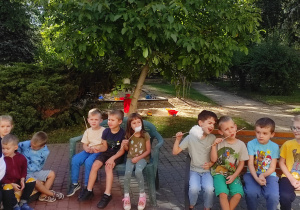 Troje dzieci z grupy Pszczółki i czterech chłopców z grupy Mrówki siedzą na ławce w ogrodzie z watą cukrową