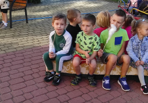 Kilkoro dzieci z grupy Mrówki siedzi na ławce w ogrodzie z watą cukrową
