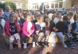 Kilkoro dzieci z grupy Ważki siedzą na ławce w ogrodzie z watą cukrową